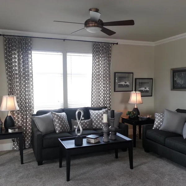 Living room of a manufactured home features a dark sofa, matching loveseat, and patterned curtains.
