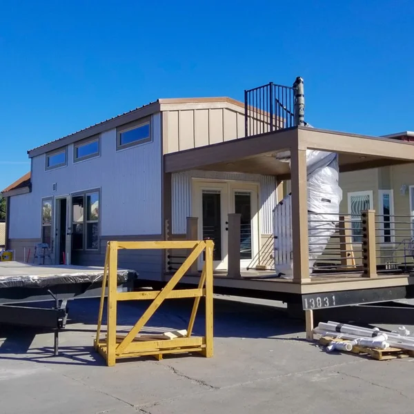 New white and beige park model tiny home with corrugated siding and rooftop patio is staged on its trailer.