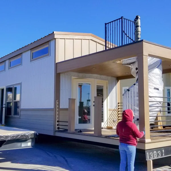 A beige and white park model home with a small roof deck is being inspected under a bright blue sky.