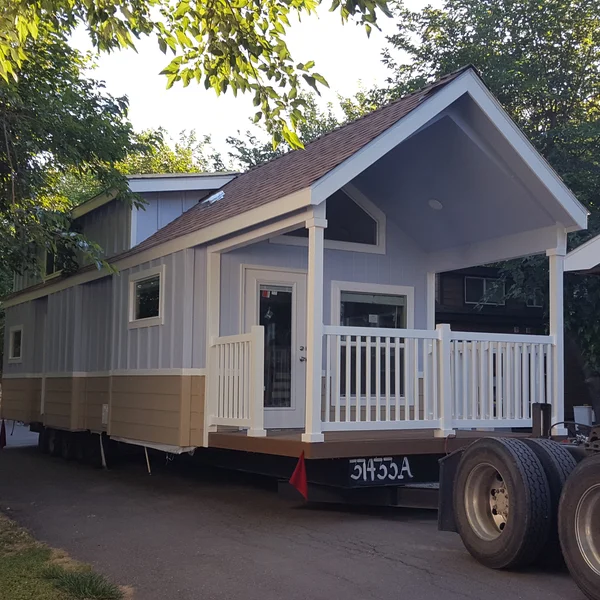 This custom park model tiny home, featuring a spacious front porch and stylish dual-tone siding, is pictured during delivery.