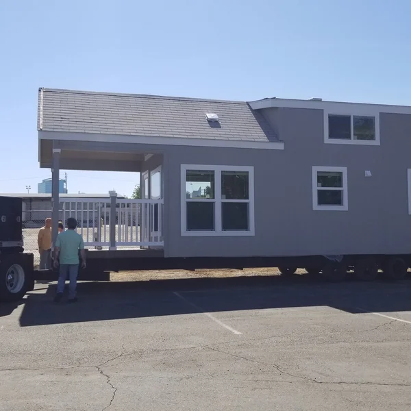 Delivery of a modern gray park model tiny home featuring a built-in covered front porch, ideal for use as a backyard ADU.