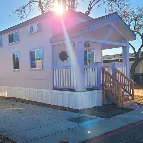 Exterior view of a light purple park model home with a porch and a holiday wreath on a sunny day.
