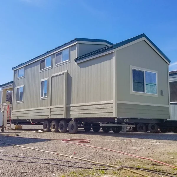 A beige, modern manufactured home, or ADU, is on a trailer outside with a blue sky overhead.
