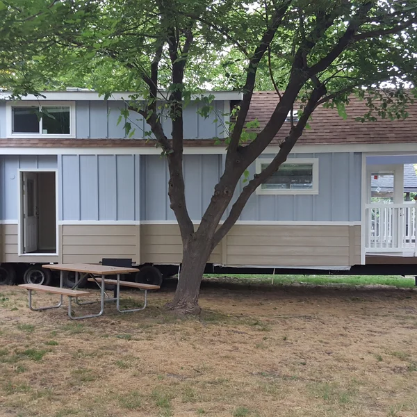 This custom park model tiny home features a two-tone exterior, cozy built-in porch, and mobile chassis designed for flexible outdoor living.