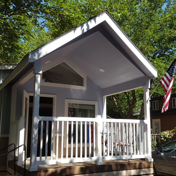 This charming park model tiny home showcases a spacious covered front porch, perfect for outdoor relaxation, complete with classic white railings.