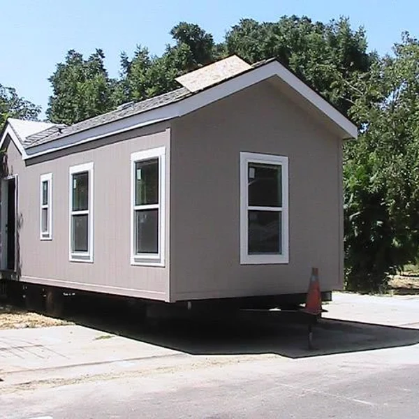 A gray prefabricated tiny home, ideal for student housing, is shown with white trim and windows on a trailer.