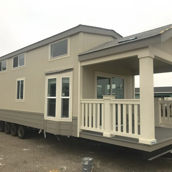 Tan park model RV tiny home with a covered porch, showcasing alternative living options and exterior design.