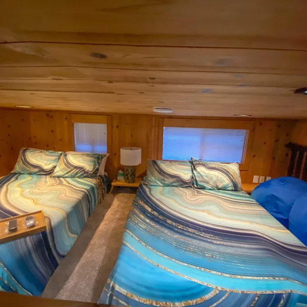 Bedroom loft in a park model or tiny home with two beds, wood paneling, and blue bedding.
