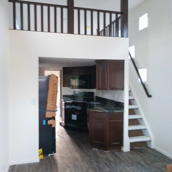 Interior of a park model home showcases a kitchen, staircase to a loft, and dark cabinetry.