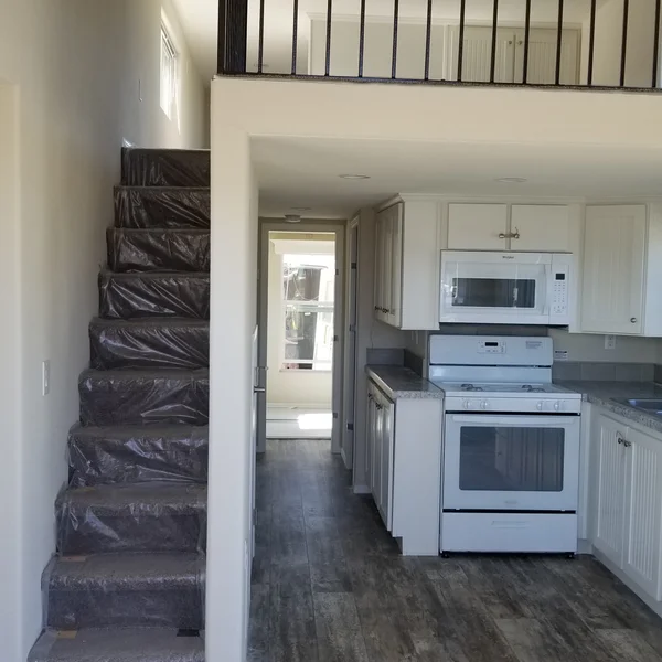 This compact tiny home kitchen features white cabinetry and modern appliances nestled under a spacious loft area, perfect for ADUs and park models.