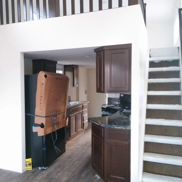 Interior of a new manufactured home showing a kitchen with dark wood cabinetry and staircase ready for occupancy.