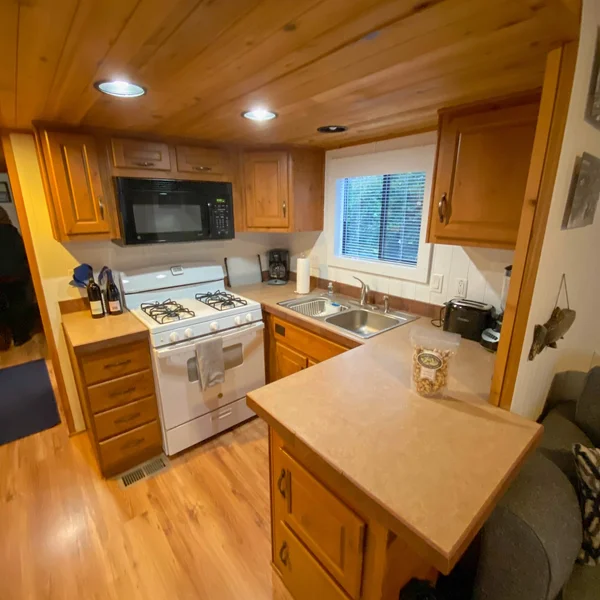 Cozy park model kitchen featuring wood cabinets, laminate countertop, white gas range and a double-basin stainless steel