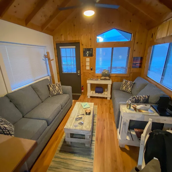 Cozy living area in a tiny home features wood walls, blue sofas, and light-colored wood furniture.