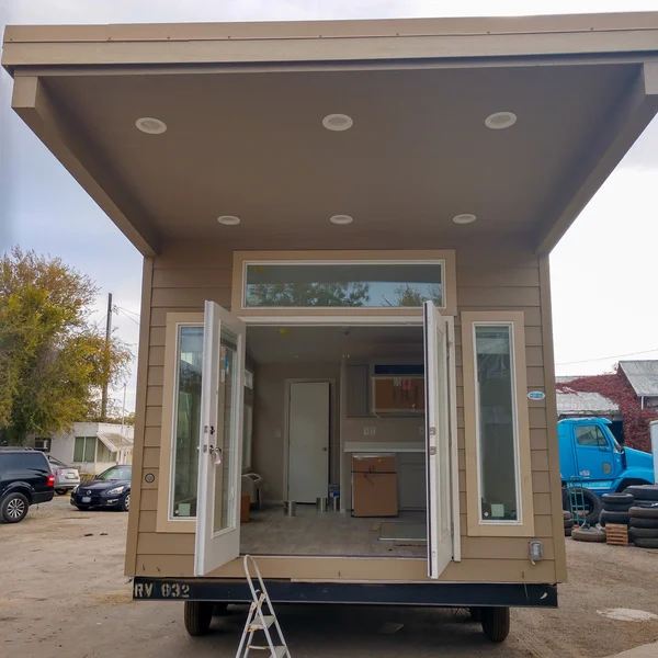 Exterior view of a brown park model tiny home with open French doors and recessed lighting.