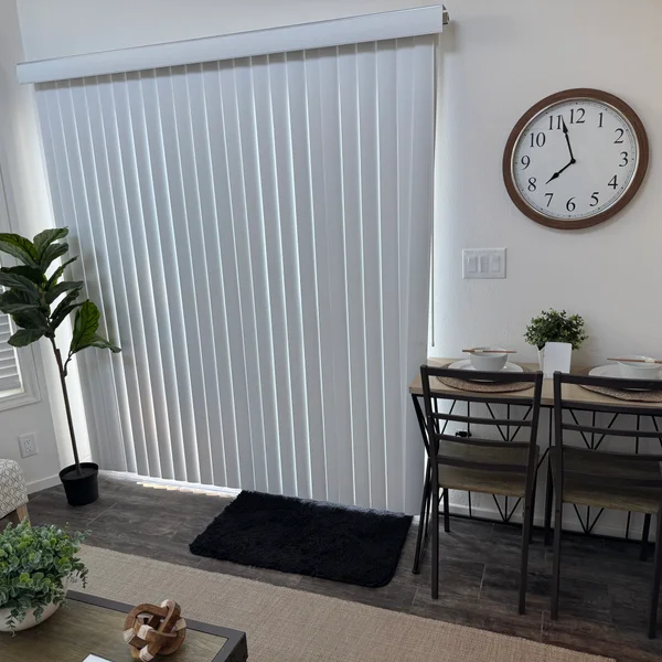 A modern dining area with white vertical blinds, black rug, round clock, and wood-grain dining table for real estate listing.