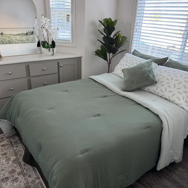 Bedroom features a green comforter, dragonfly-patterned pillows, potted plant, and gray dresser near a window.