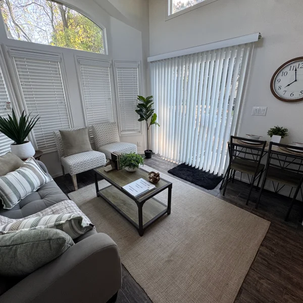 Bright real estate living room featuring a gray sofa, chairs, coffee table, and large windows with white blinds.
