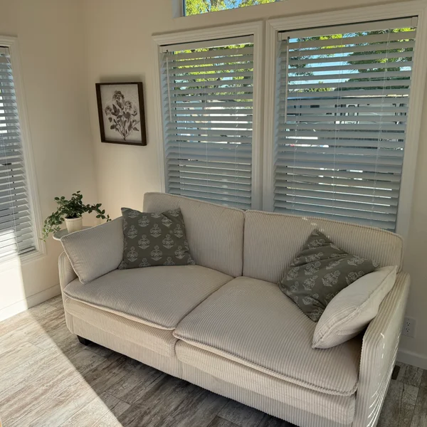Real estate staging: Cream-colored sofa with anchor pillows sits in a bright room with sunlight streaming through window
