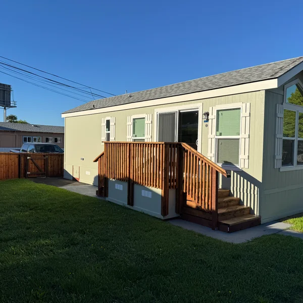 Real estate listing shows a light green mobile home with wood deck and steps, with green lawn.