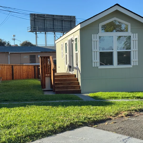 Charming mobile home with wooden steps, white shutters, and green lawn offers affordable real estate.