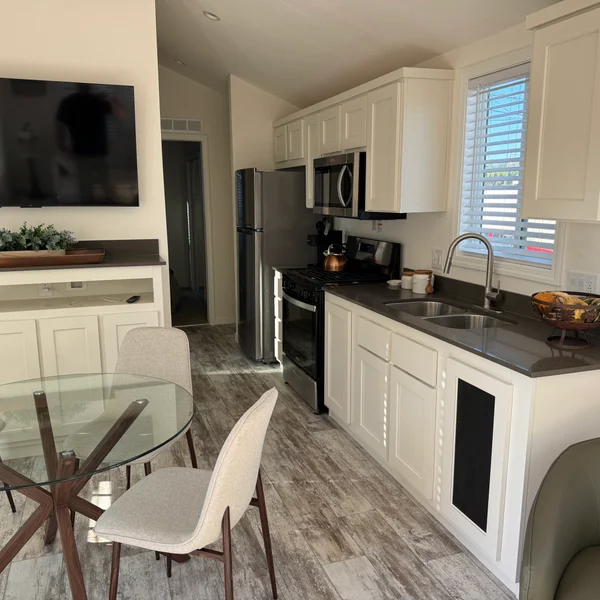 Bright, modern kitchen features white cabinets, stainless steel appliances, dark countertops, and a glass-top table.