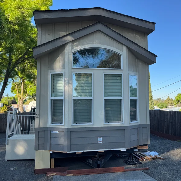 Exterior view of a newly constructed, light gray manufactured home with large windows for real estate listing.