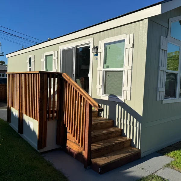Exterior of a green mobile home with wooden steps and a deck, showcasing real estate property.
