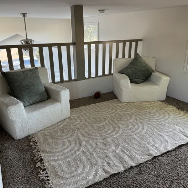 Cozy loft area features two white armchairs, green pillows, and patterned rug, showcasing a home's potential.