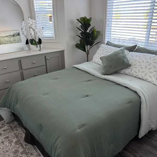 A light-filled bedroom features a bed with a green comforter, a gray dresser, and a fiddle-leaf fig tree.